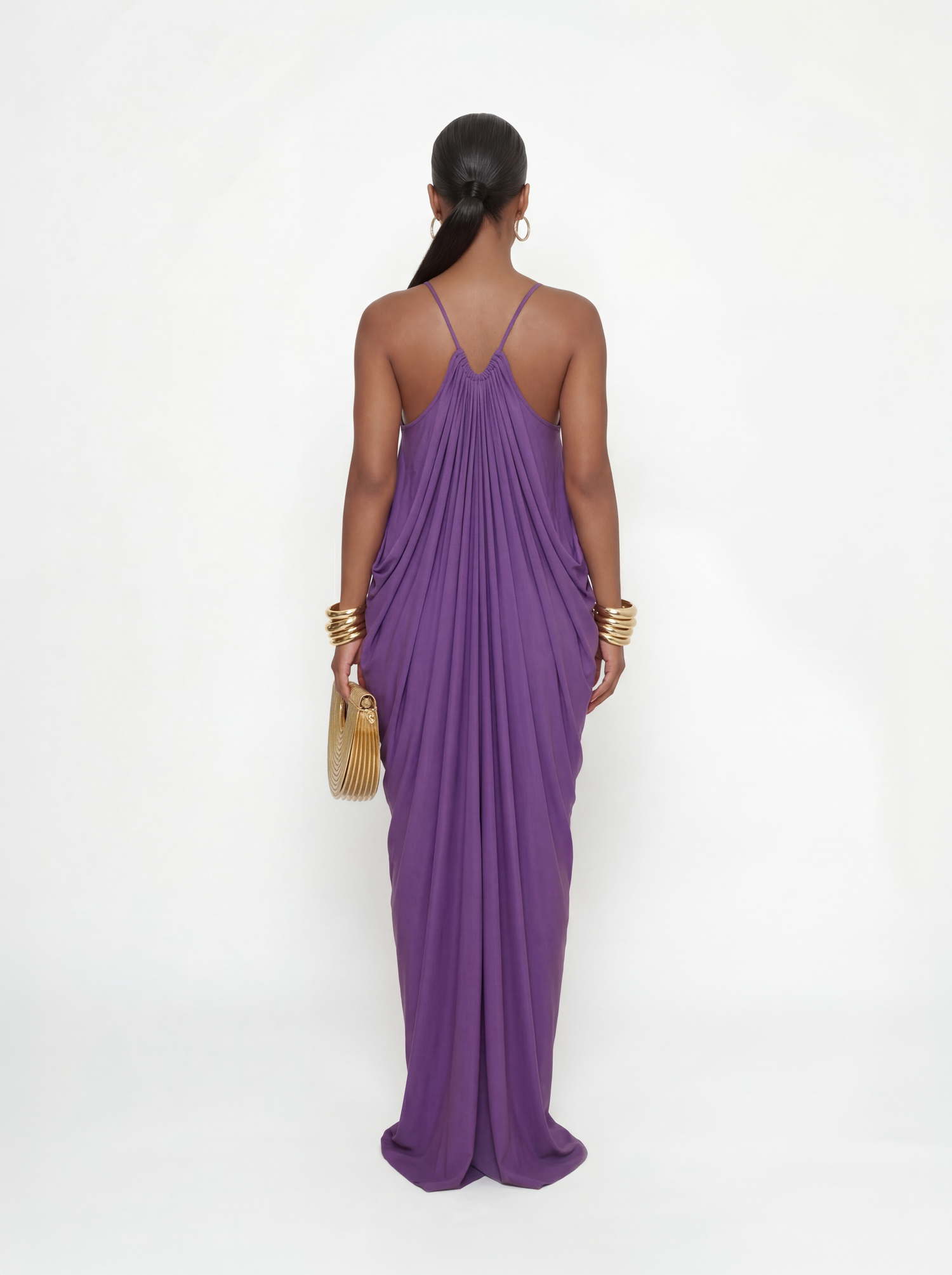 Back view of a purple flowy maxi dress with a low back and thin straps, showcasing a draped silhouette and full-length design.