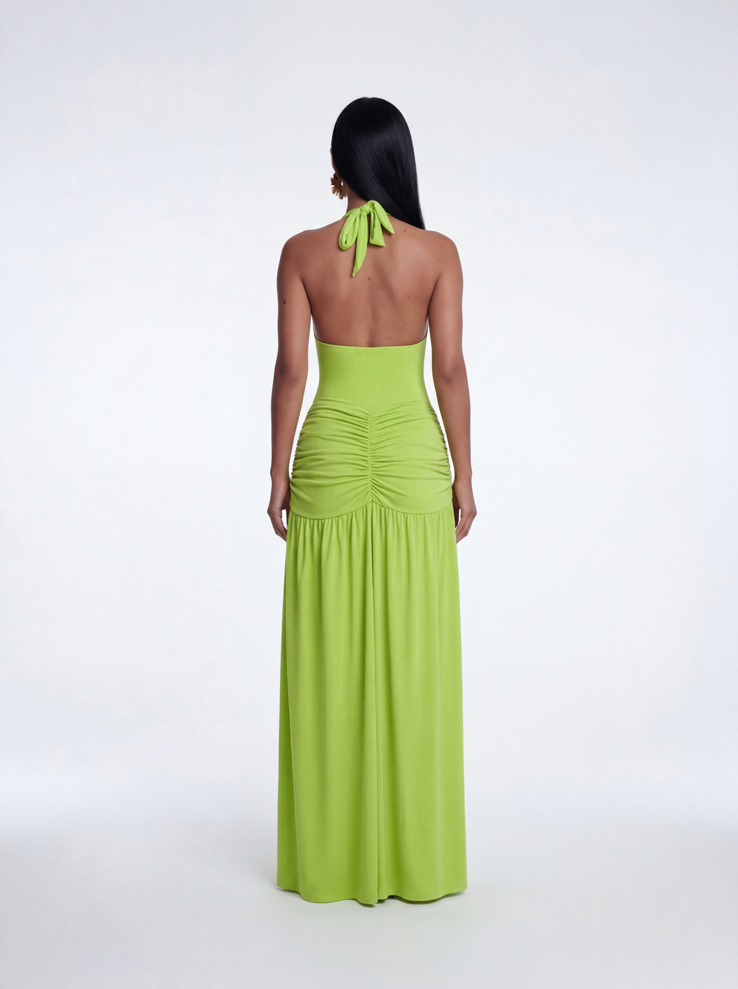 Back view of a lime green halter one-piece with a fitted silhouette and ruched skirt detail flowing into a full-length draped skirt.