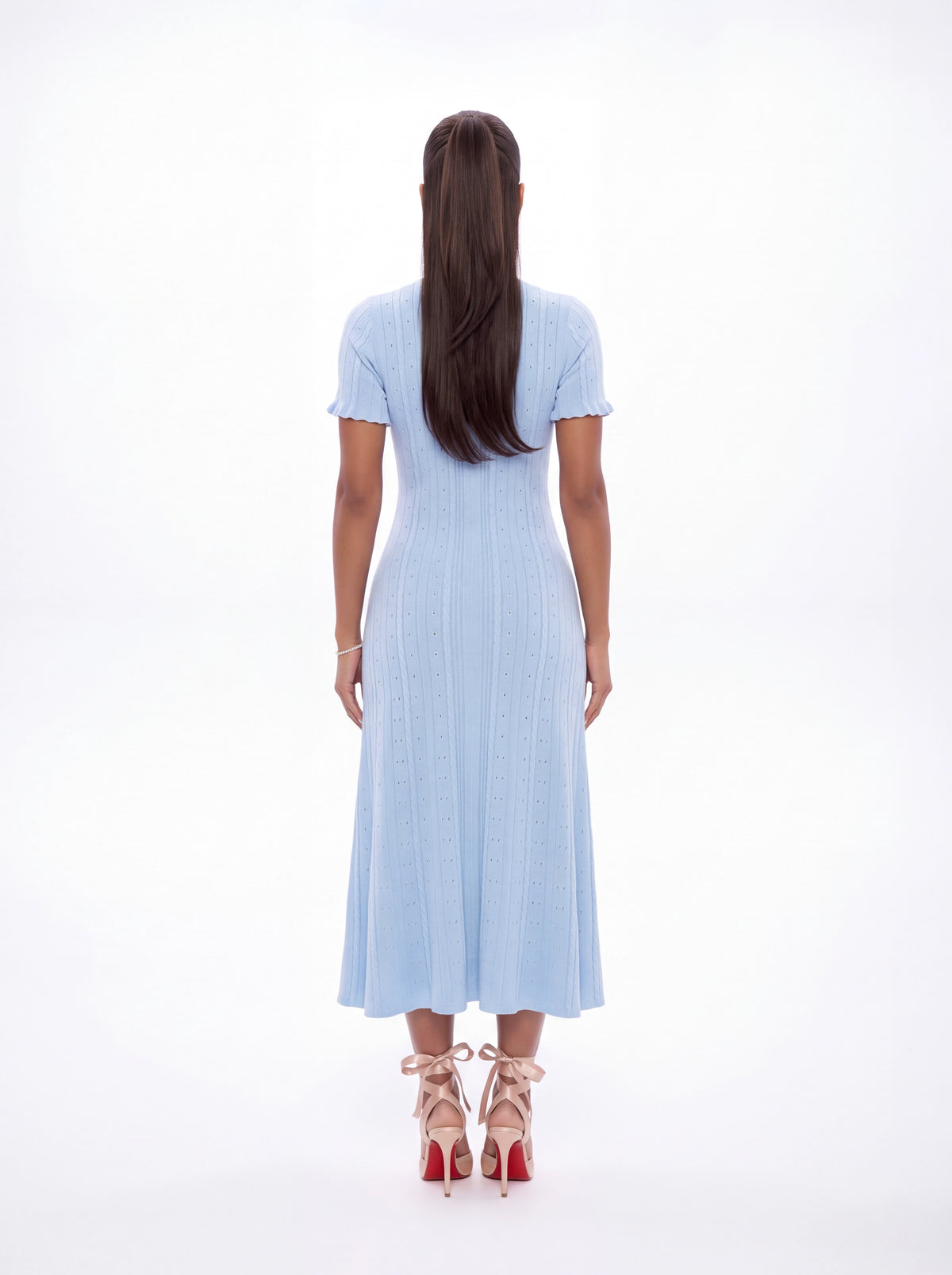 A woman viewed from behind wearing a light blue short-sleeve midi dress with a textured vertical stripe pattern and scalloped edges, paired with red high-heeled sandals against a white studio background.