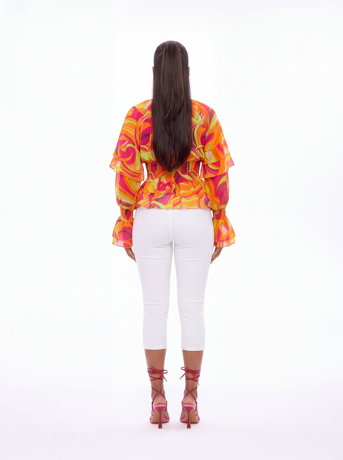 Back view of the Vera Floral Top in coral, showing the smocked waist, layered ruffle sleeves and flared cuffs in an orange and pink swirl print.