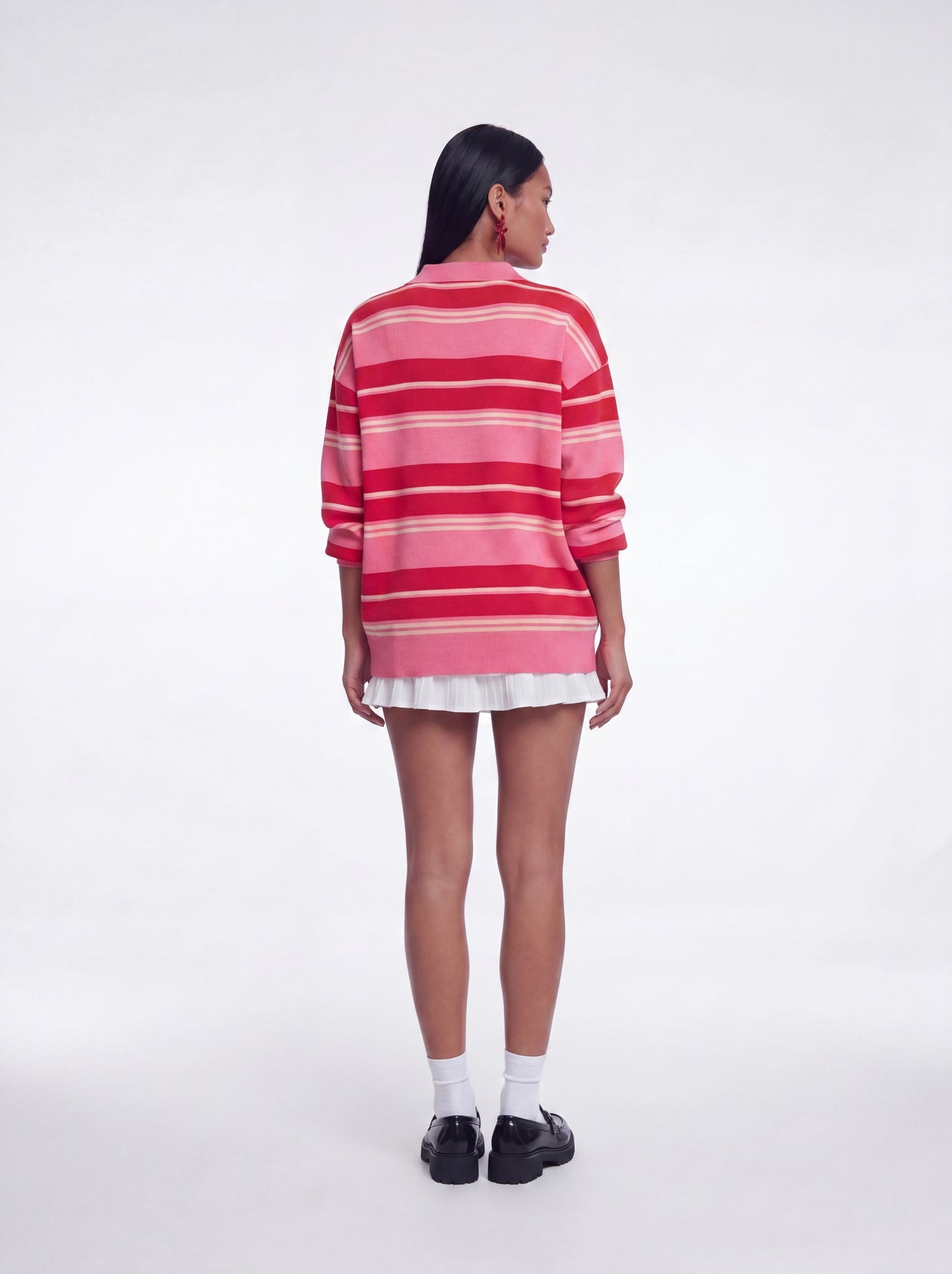 Back view of oversized pink and red striped knit sweater top featuring long sleeves, relaxed oversized silhouette, and collared neckline paired with a white layered mini skirt and black loafers.