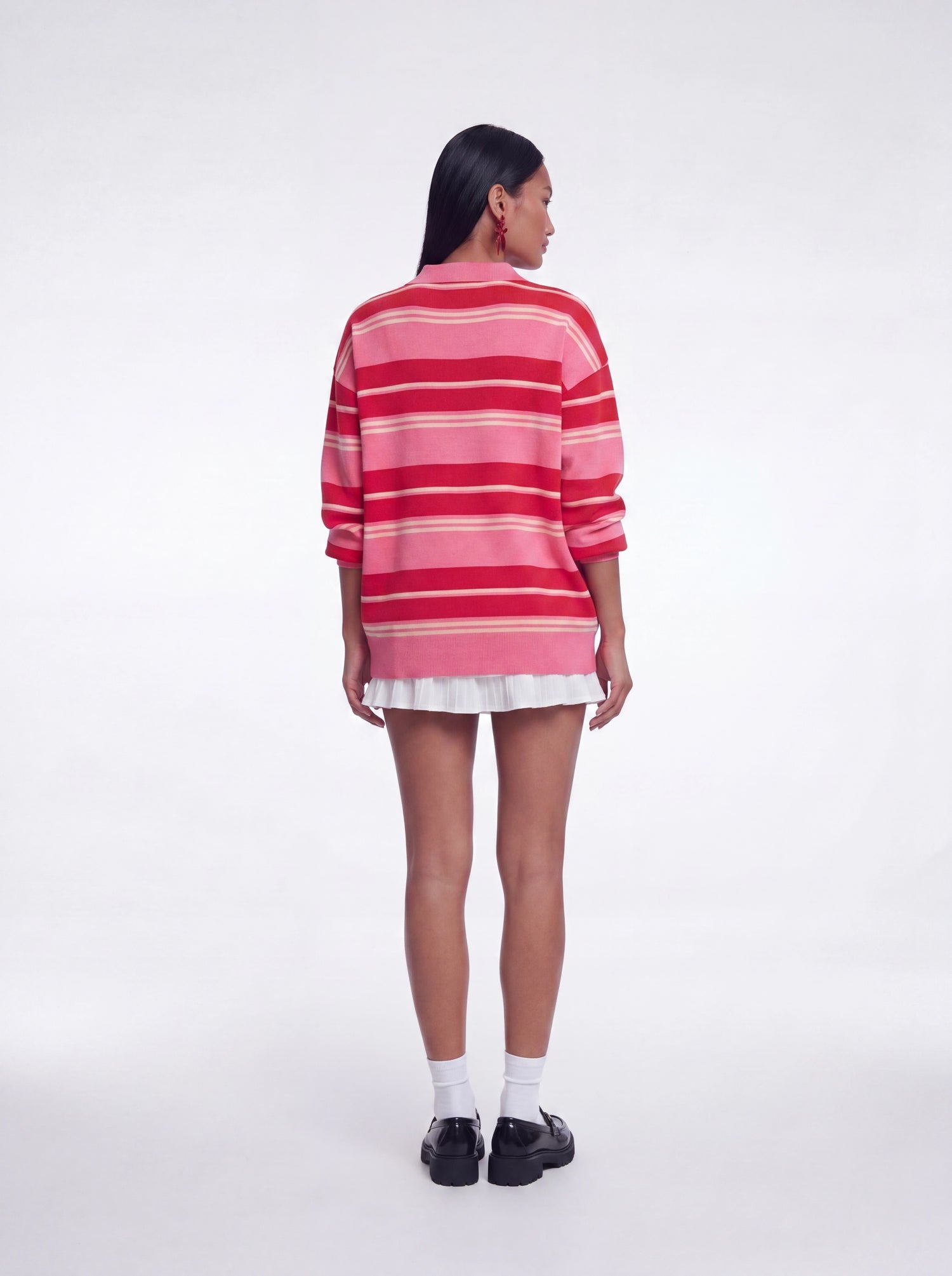 Back view of oversized pink and red striped knit sweater top featuring long sleeves, relaxed oversized silhouette, and collared neckline paired with a white layered mini skirt and black loafers.
