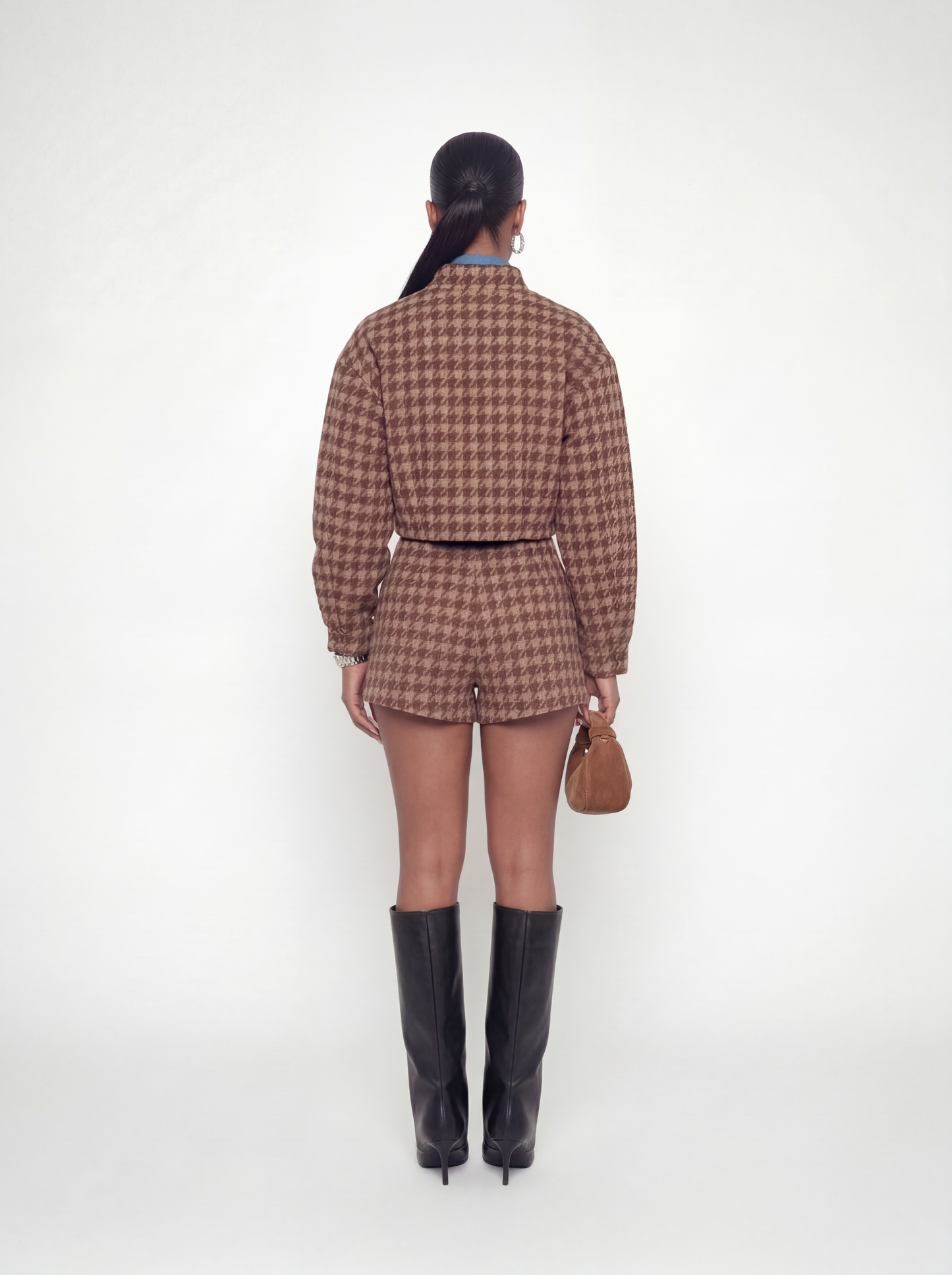 Woman wearing a brown checkered outfit with black boots on a white background