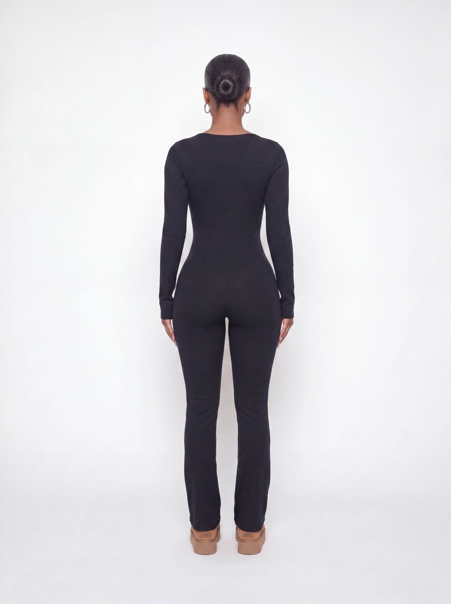 Back view of a black ribbed long sleeve jumpsuit featuring a body-contouring fit, full-length legs, and soft stretchy ribbed fabric.