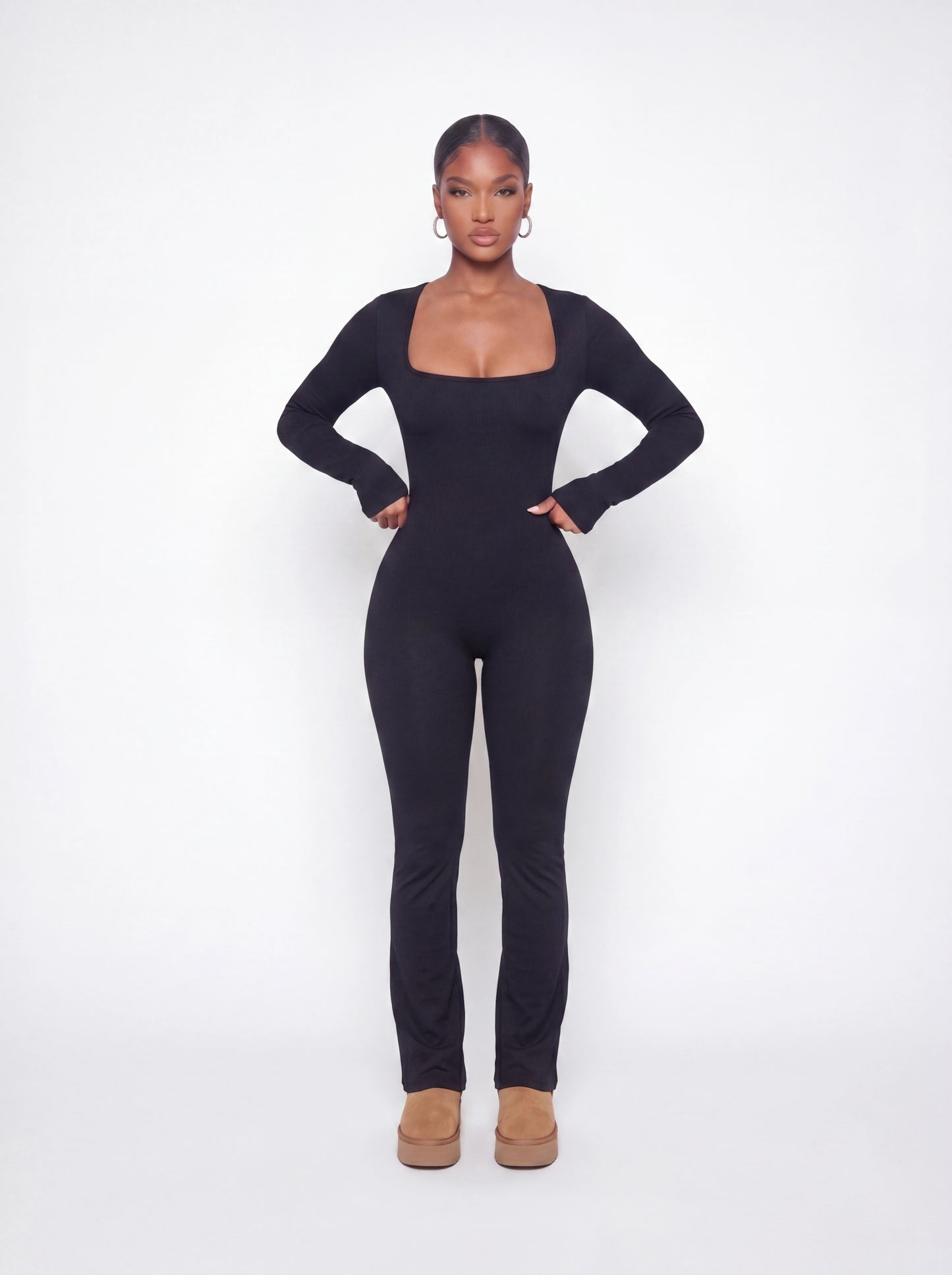 Model wearing a black long sleeve ribbed jumpsuit with a square neckline, curve-hugging fit, and full-length silhouette in soft stretchy fabric.