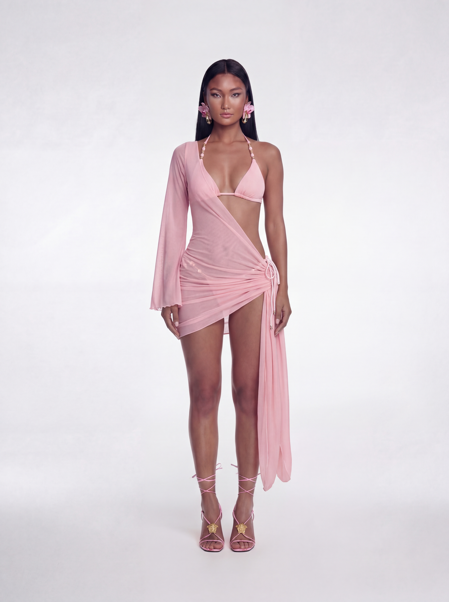 Woman wearing a pink dress with long sleeves and a draped design on a white background