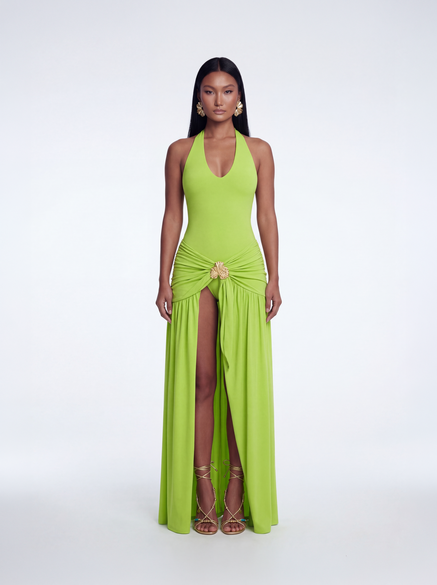 Model wearing a lime green halter one-piece swimsuit with a draped maxi skirt featuring a high slit and gold hardware detail at the waist.