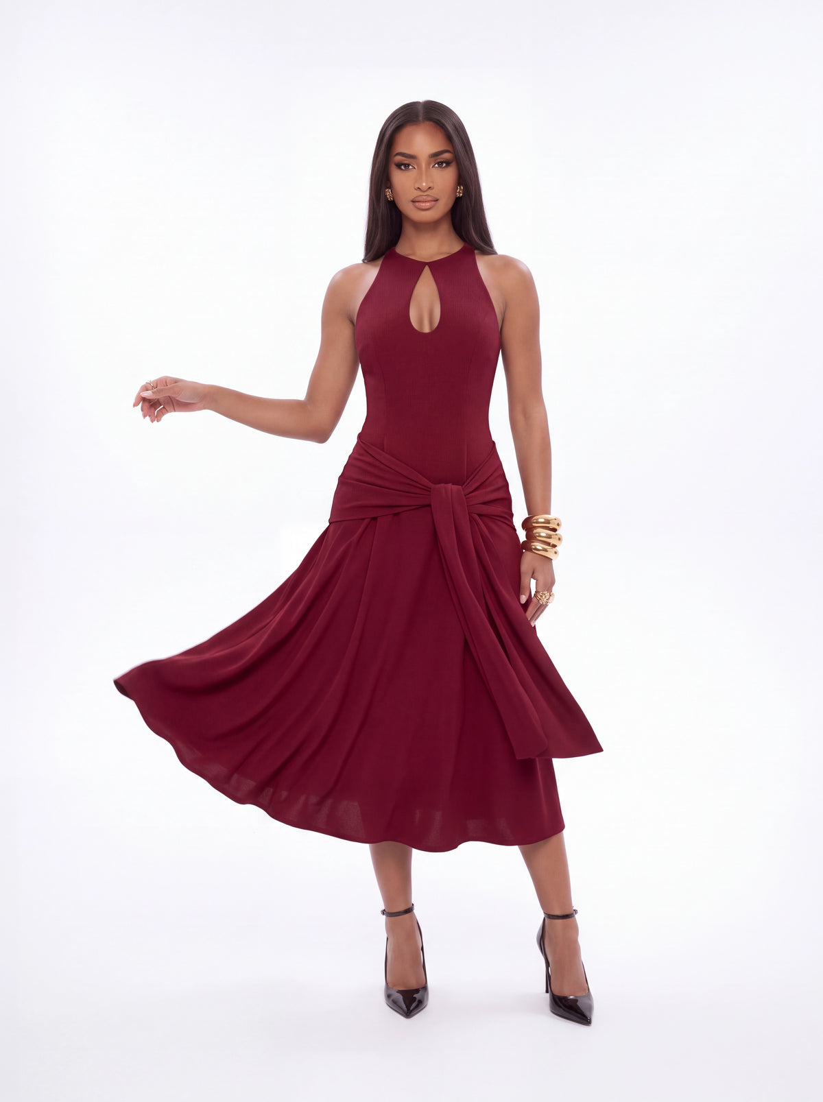 A woman modeling a sleeveless, high-neck, midi-length wine red dress with a keyhole cutout at the chest, a gathered waist, and a flowing skirt, set against a plain white studio background.
