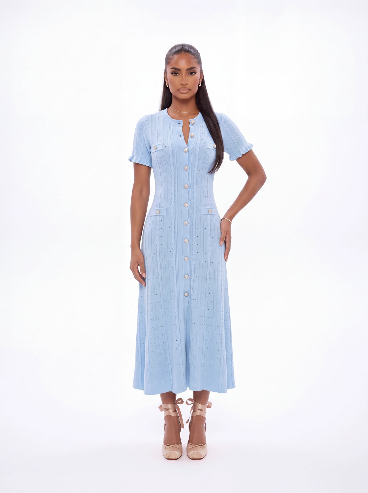 A woman modeling a light blue short-sleeve midi dress with a button-up front, standing against a plain white studio background.