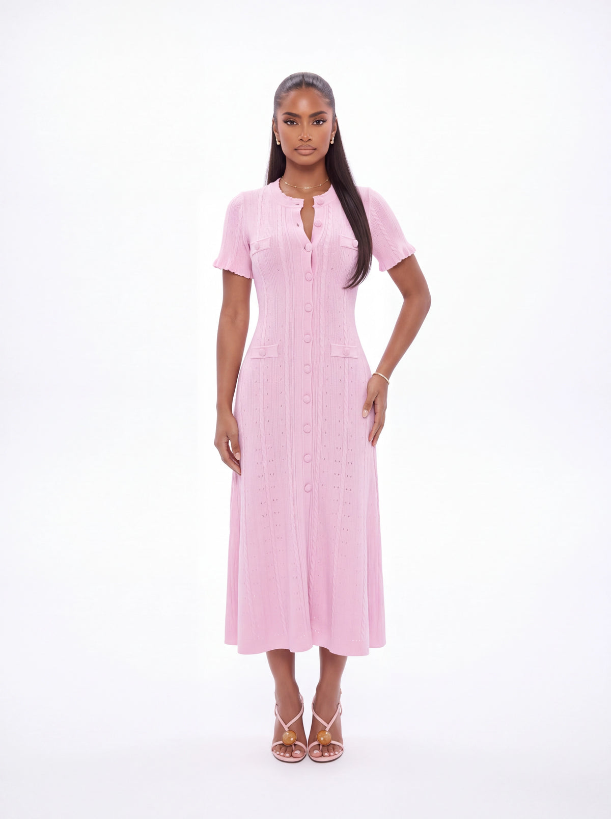 A woman modeling a light pink short-sleeve midi dress with a button-down front and vertical textured stripes, standing against a plain white studio background.