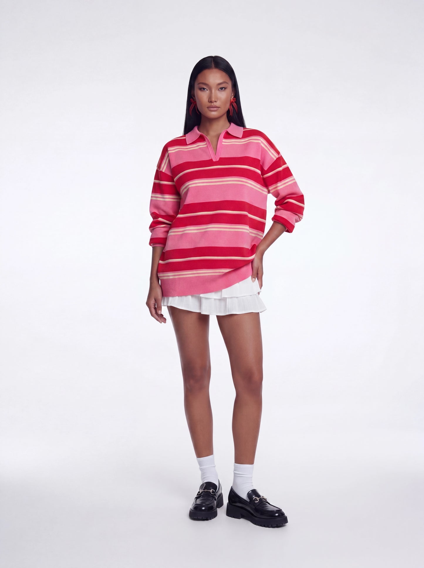 Model wearing an oversized pink and red striped collared knit sweater top with long sleeves and a relaxed fit paired with a white layered mini skirt and black loafers.