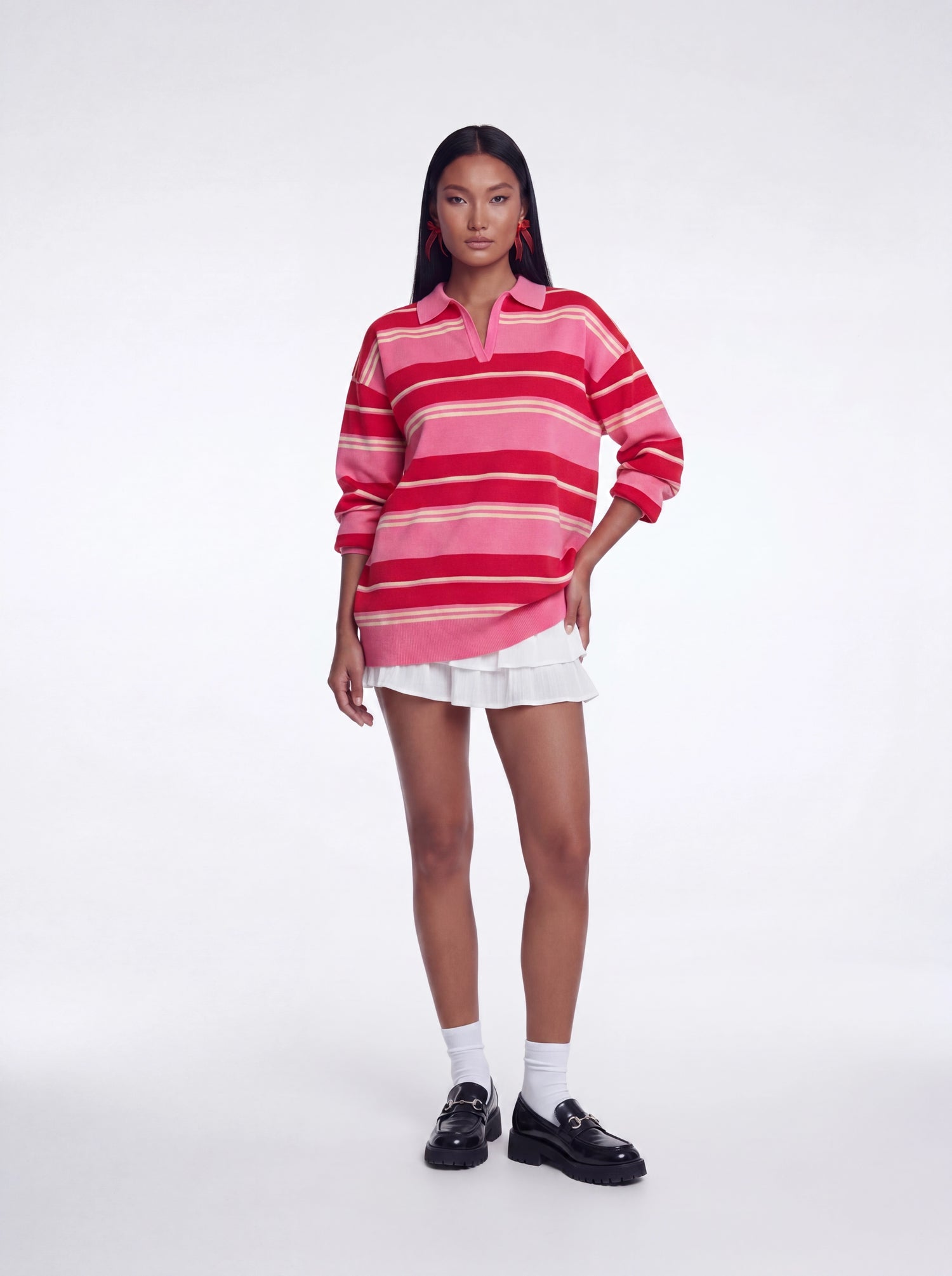 Model wearing an oversized pink and red striped collared knit sweater top with long sleeves and a relaxed fit paired with a white layered mini skirt and black loafers.