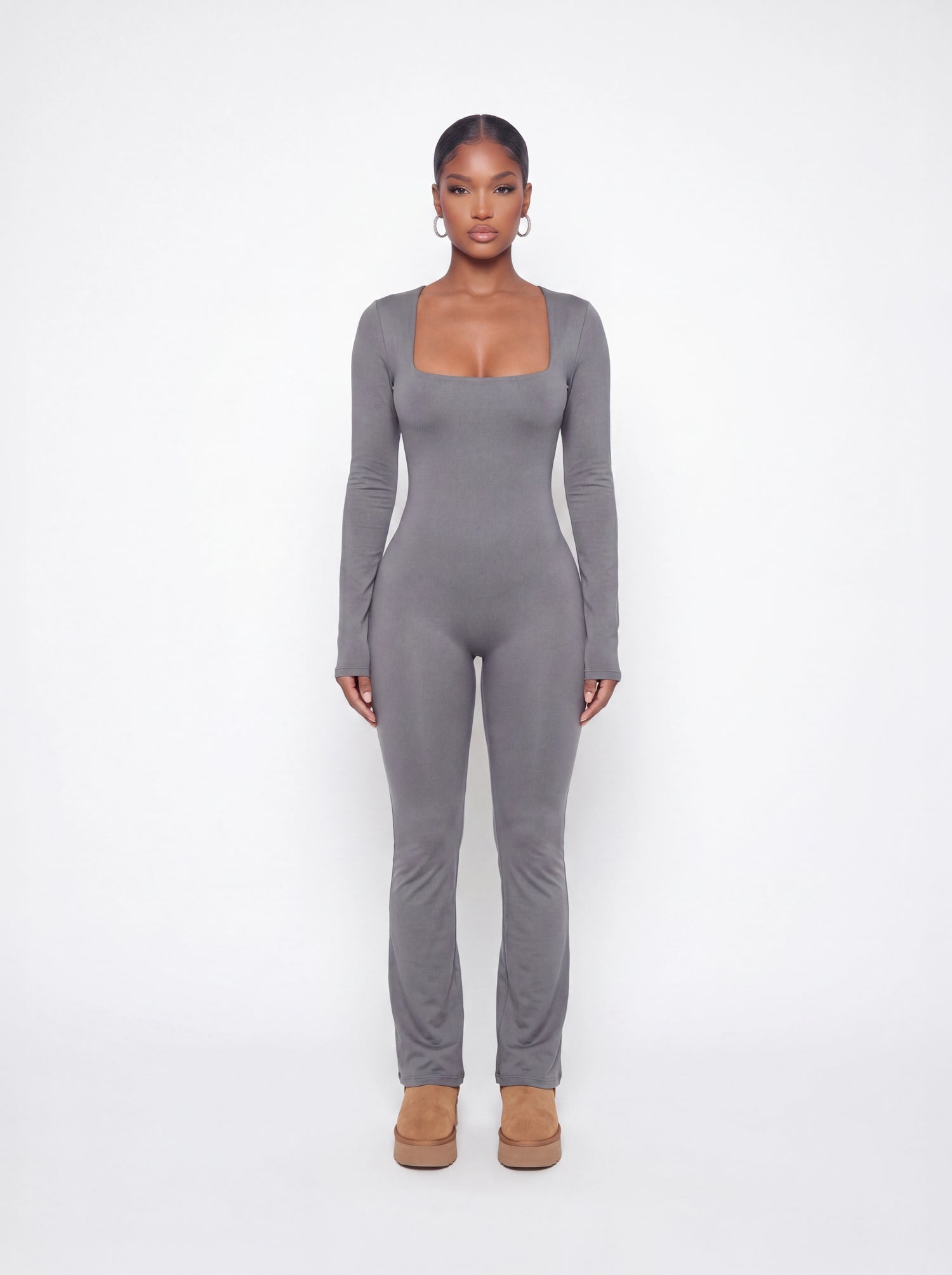 Model wearing a grey long sleeve ribbed jumpsuit with a square neckline, curve-hugging fit, and full-length silhouette in soft stretchy fabric.
