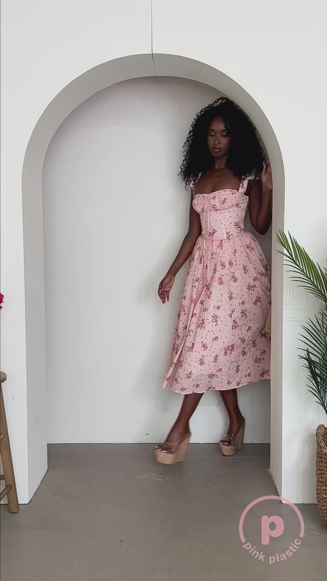 Video of a model wearing a blush pink floral corset midi dress with a ruched sweetheart neckline, ruffled shoulder straps, and a full gathered skirt.