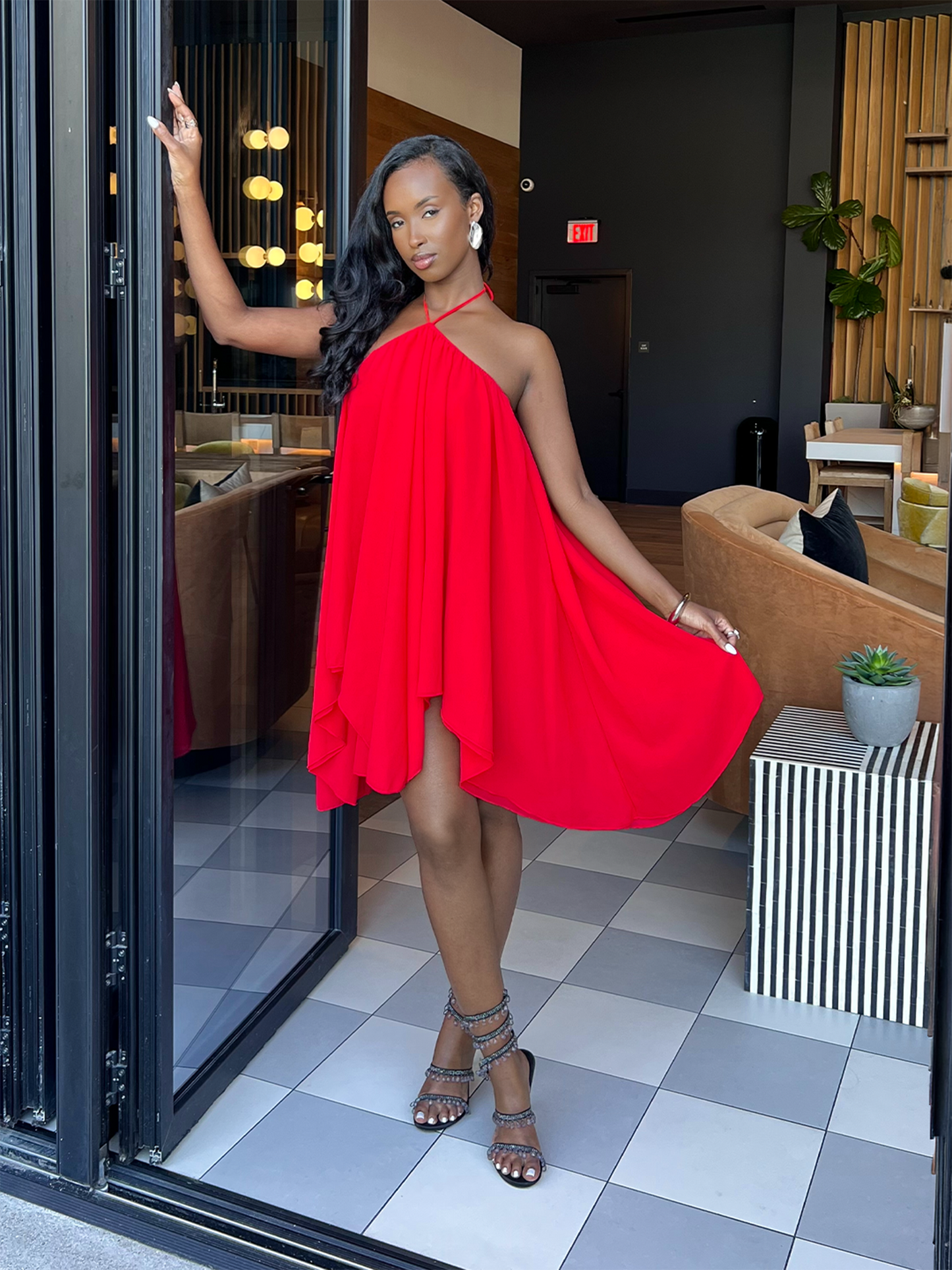 Model in a red dress standing in a modern indoor setting with a checkered floor.