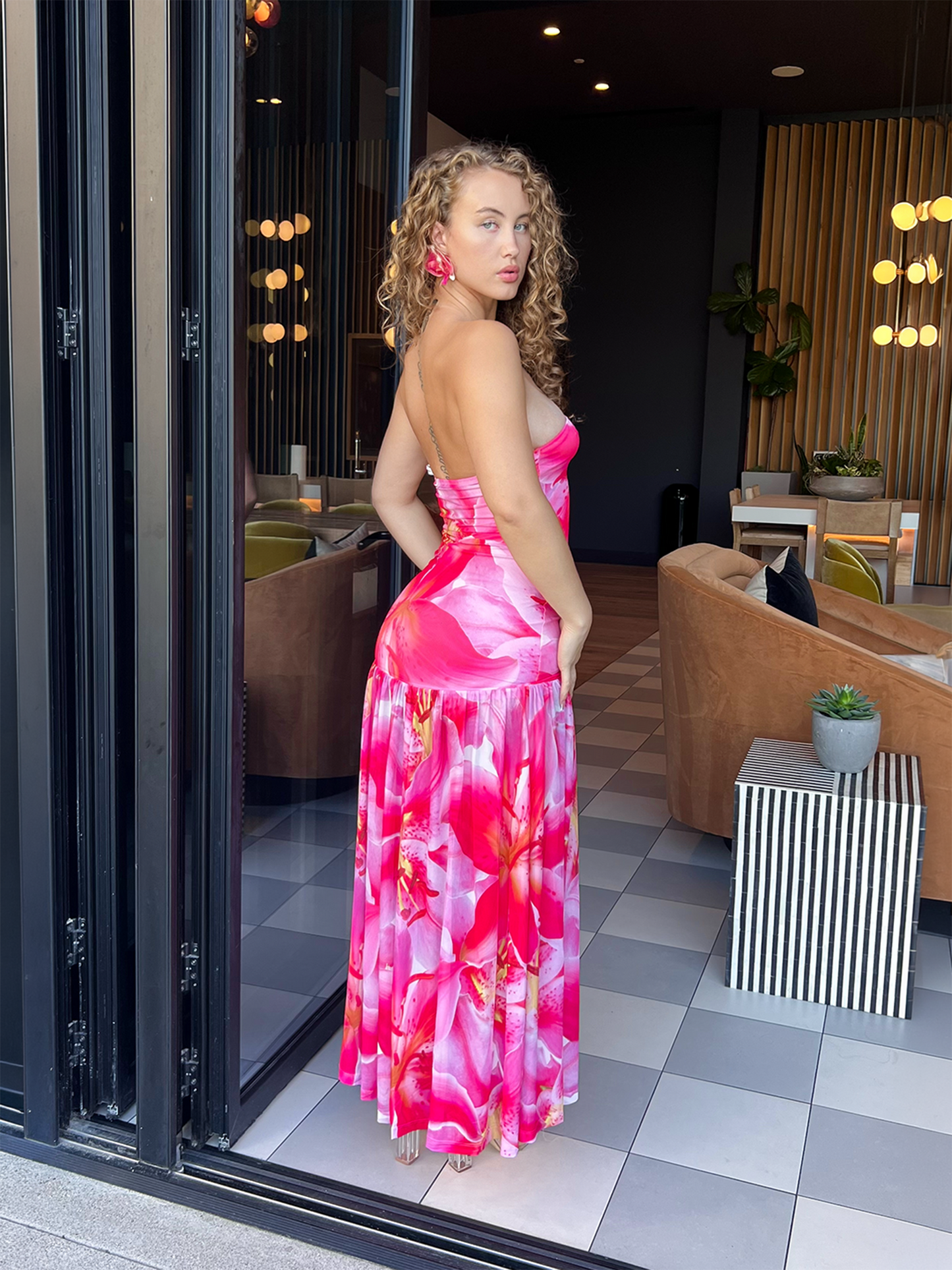 Model wearing a strapless pink floral maxi dress with a fitted bodice and drop waist, shown from the back with a flowy skirt.